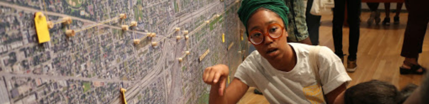 Person points at large aerial photo map with pushpins and tags.